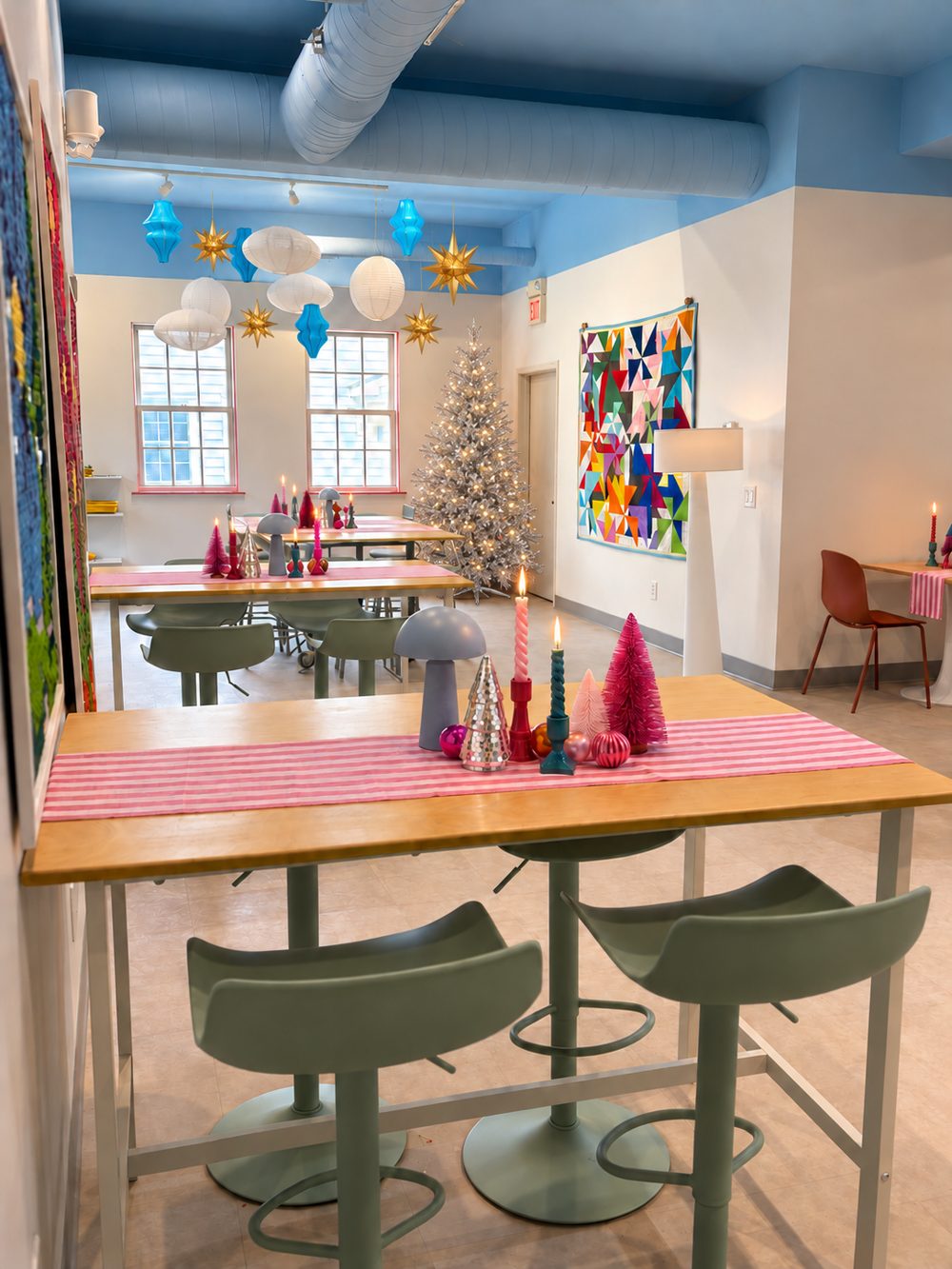 Atelier Collective studio decorated for the holidays, with a silver tree, paper lanterns and candles on striped table runners